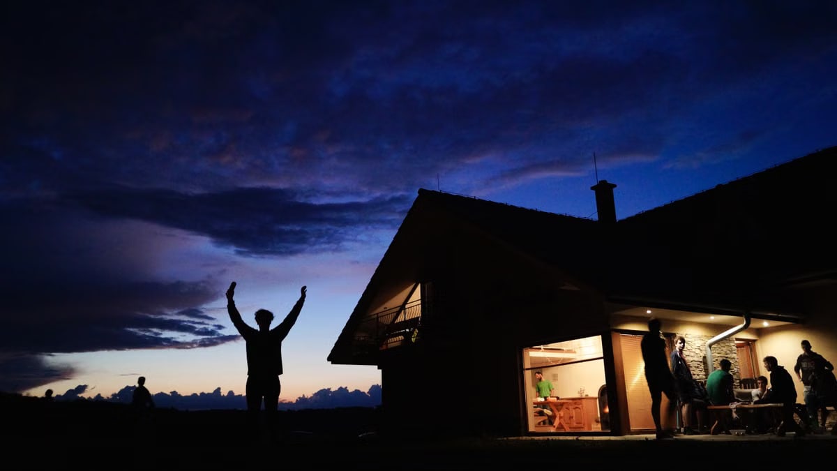 People gathered at a cozy cottage during twilight, enjoying the evening outdoors and indoors.